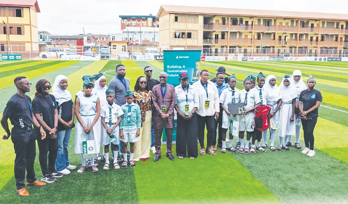 Students and programme representatives standing together on a sports pitch in Lagos, with some students holding donated items