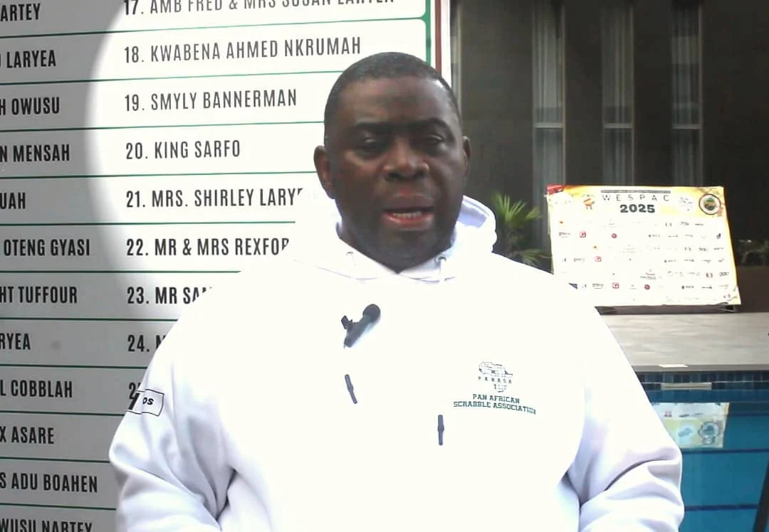 Adekoyejo Adegbesan wearing a white Pan African Scrabble Association top while speaking