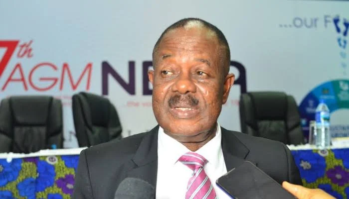 Ifeanyi Okoye wearing a dark suit and pink striped tie while speaking at an event