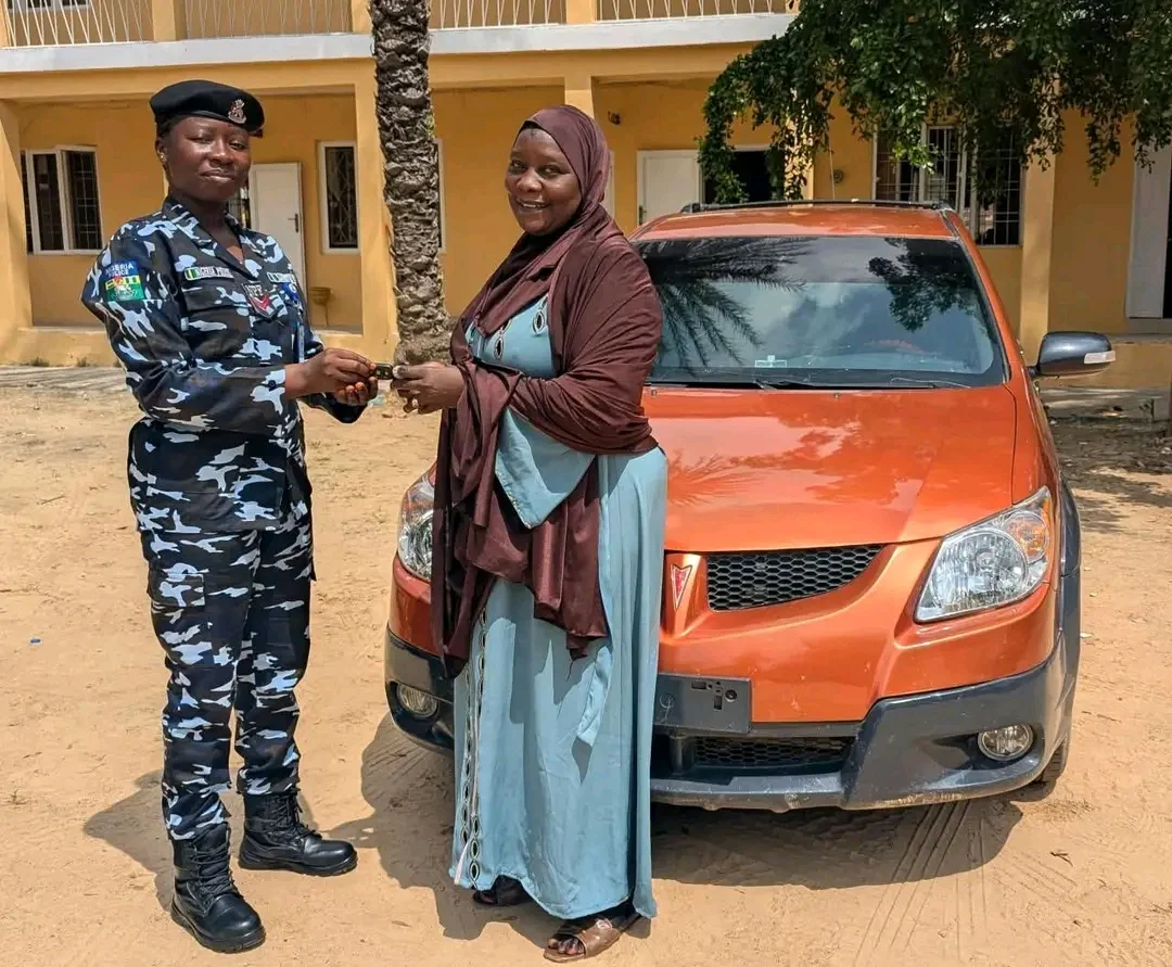 A police officer handing a key to a woman beside an orange car at the Kano police headquarters