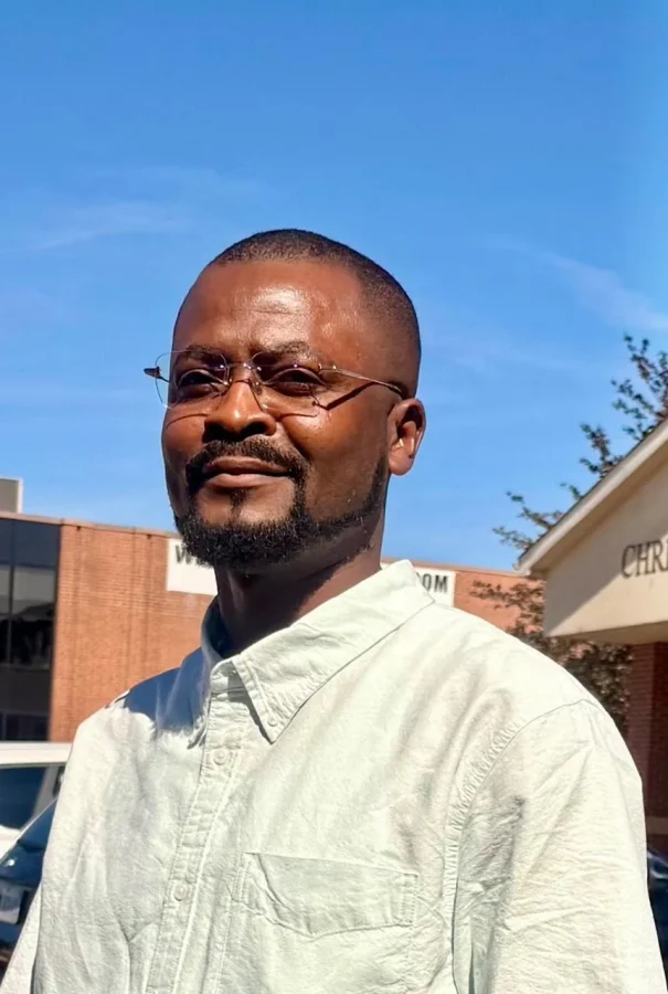 Olola Daniel wearing glasses and a light-coloured shirt while standing outdoors