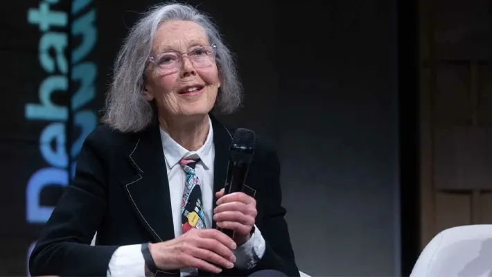 Anne Carson seated on stage holding a microphone