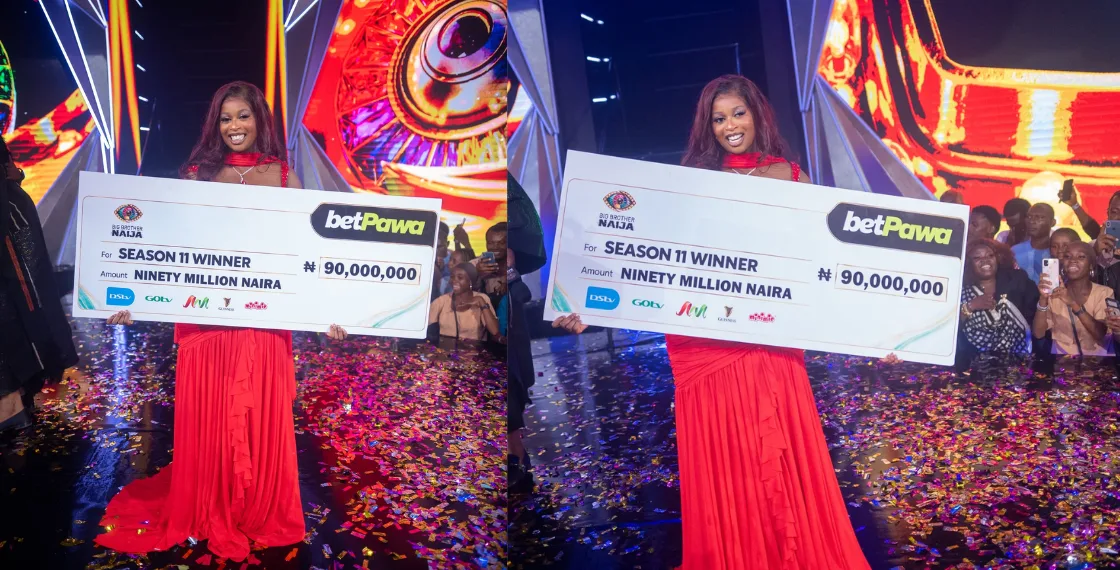 Temi Nkem in a red dress holding a large Season 11 winner cheque for ₦90 million on stage